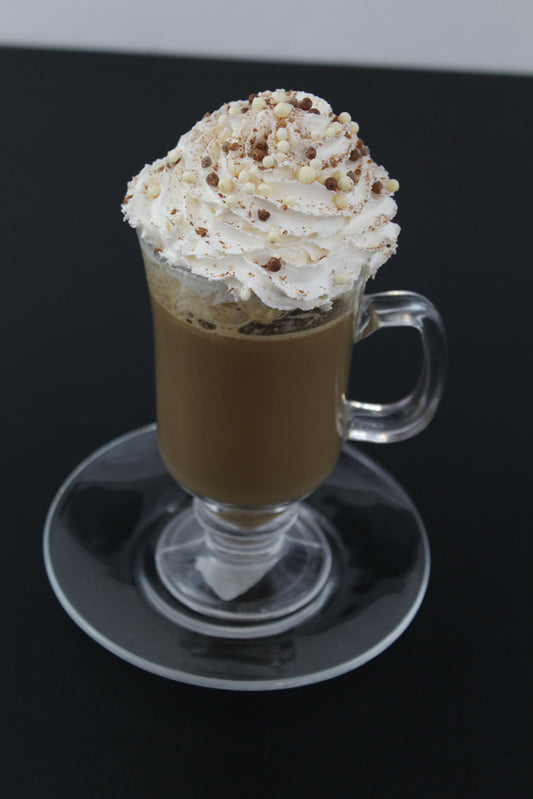 A clear glass mug filled with dark coffee topped with a swirl of whipped cream and chocolate sprinkles sits on a round glass plate against a black background.