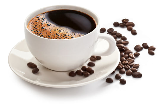 A white coffee cup filled with dark, frothy coffee sits on a saucer, surrounded by scattered coffee beans on a bright background.