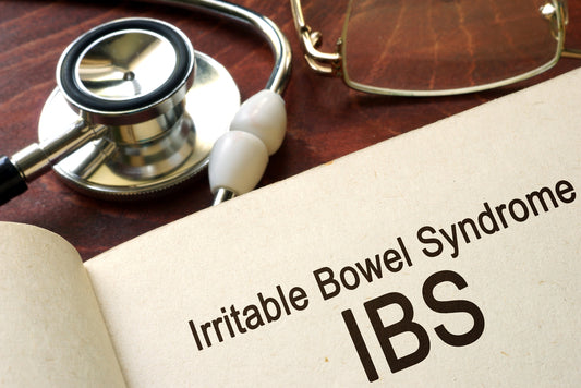 A stethoscope rests beside an open book displaying the text "Irritable Bowel Syndrome" and its abbreviation "IBS," on a wooden surface.