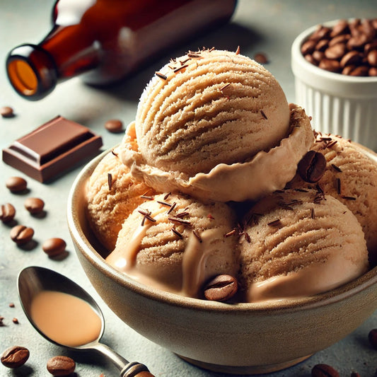 A bowl of creamy coffee-flavored ice cream scoops is topped with chocolate shavings and surrounded by coffee beans, a chocolate square, and a bottle, set against a textured surface.