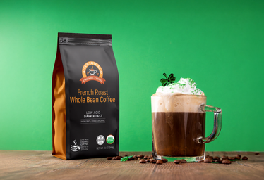 Coffee bag and cup of coffee with whipped cream on a wooden surface against a green background