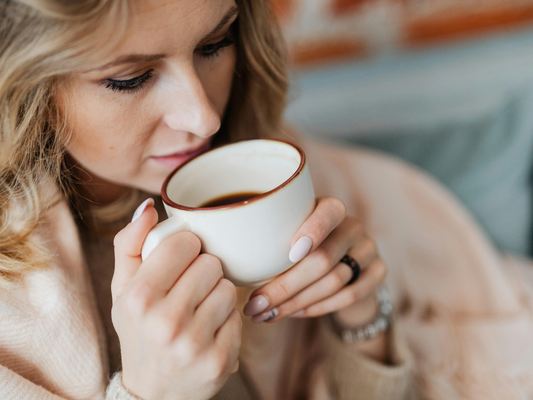 Woman holding a warm cup of coffee close to her face, enjoying the aroma in a cozy indoor setting