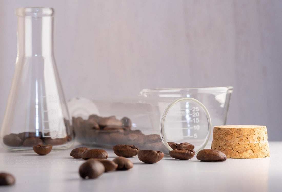 Several coffee beans are scattered on a table, with a glass beaker and a flask in the background, suggesting a scientific exploration of coffee acidity.