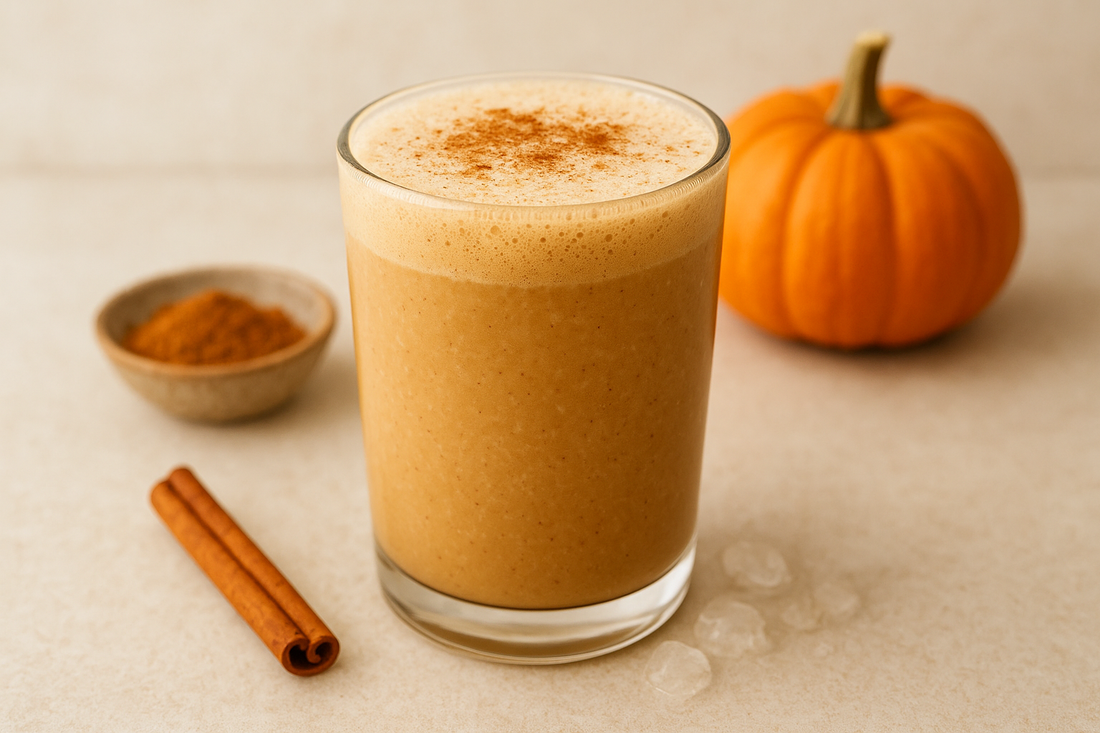 Glass of creamy pumpkin spice smoothie topped with cinnamon, surrounded by a whole pumpkin, cinnamon sticks, and a bowl of ground cinnamon — a cozy, autumn-inspired scene.