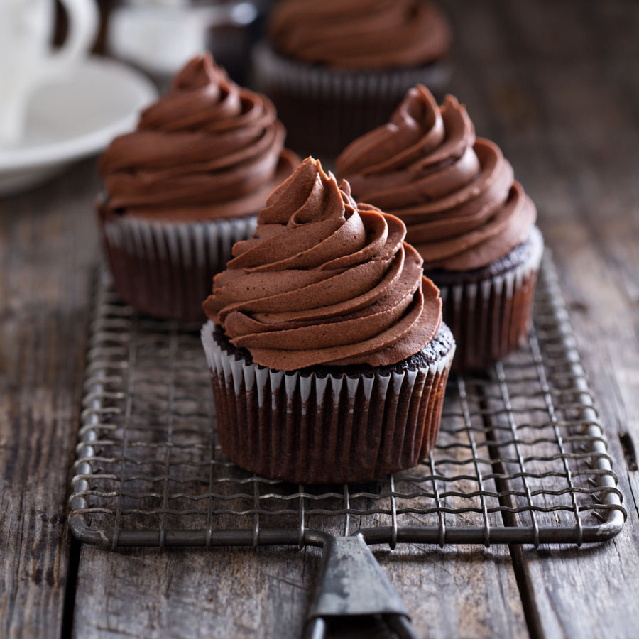 Four chocolate cupcakes with swirls of rich chocolate frosting are arranged on a wire cooling rack against a rustic wooden background.