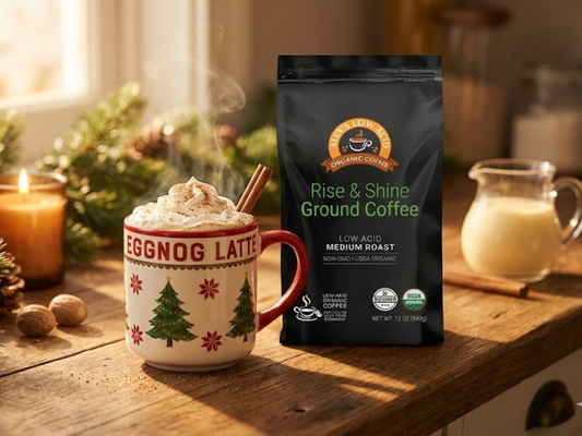 Warm eggnog latte topped with nutmeg beside Alex’s Low-Acid Coffee bag on a cozy holiday counter with pine sprigs.