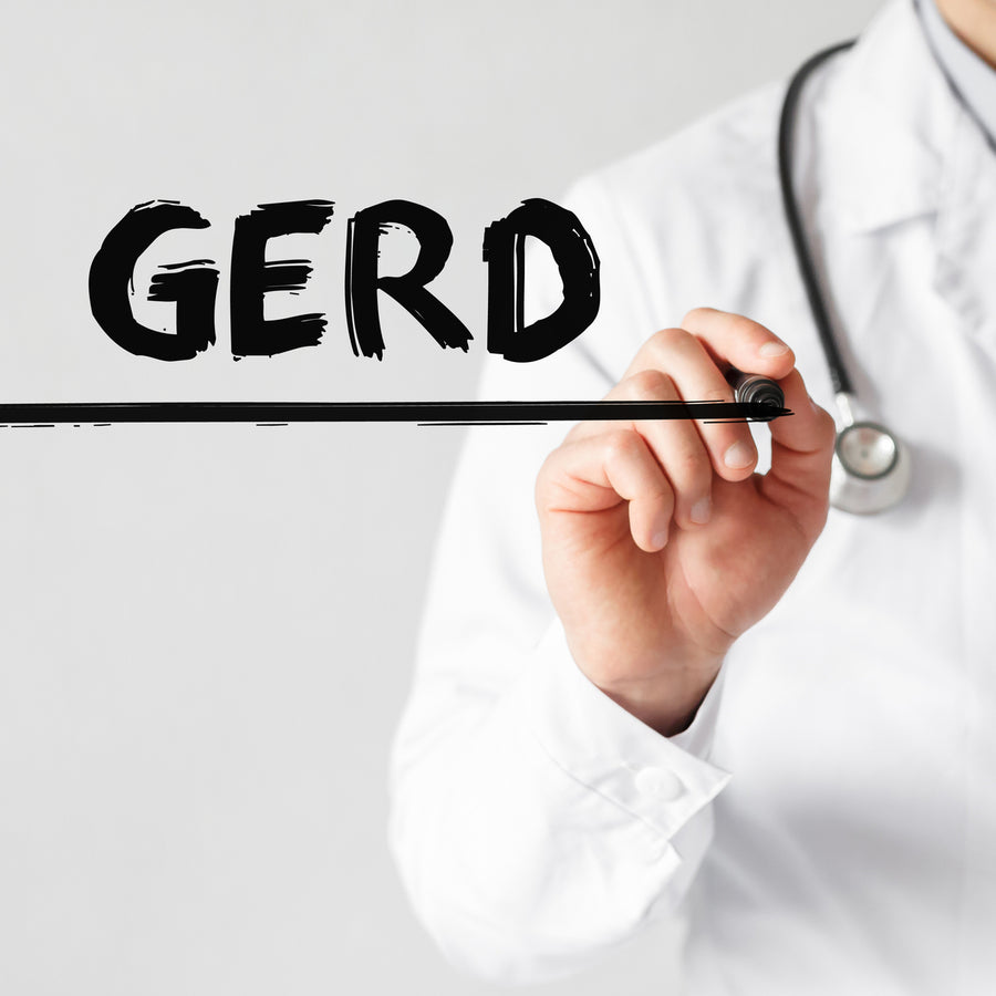 A healthcare professional in a white coat is writing "GERD" on a clear surface, highlighting the term related to a medical condition, with a stethoscope visible around their neck.