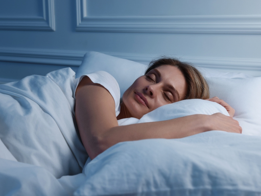 A woman sleeping peacefully on her side in a bed with white bedding in a calm, softly lit bedroom.