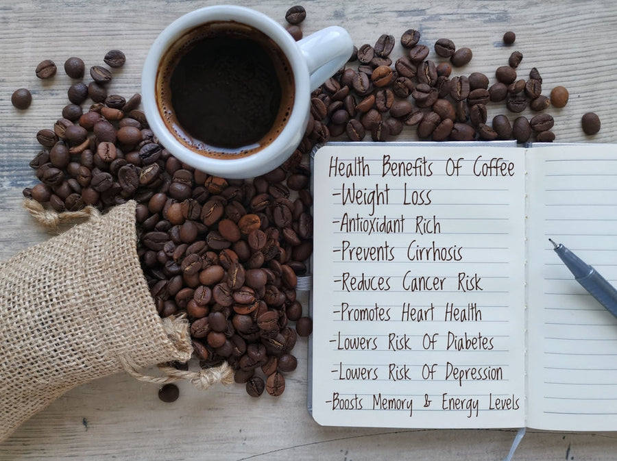 A cup of coffee sits beside a notebook filled with handwritten notes on the health benefits of coffee, surrounded by scattered coffee beans and a small burlap sack.