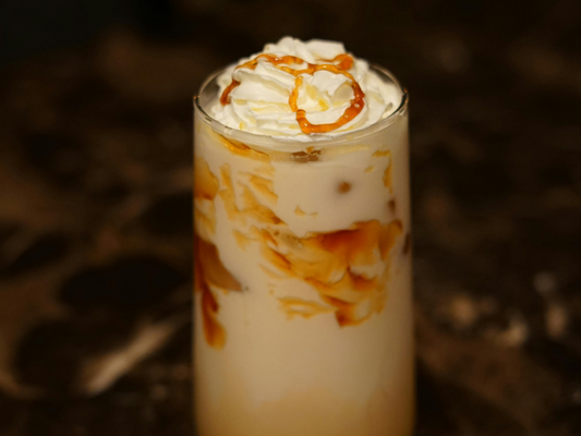 Iced caramel latte with milk and caramel swirls, topped with whipped cream and caramel drizzle in a tall glass.