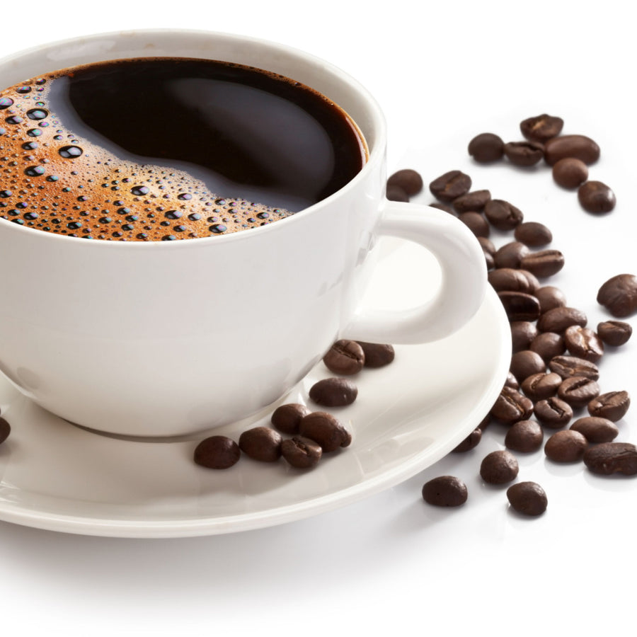 A white cup filled with dark coffee, topped with bubbles, sits on a saucer surrounded by scattered coffee beans on a white background.
