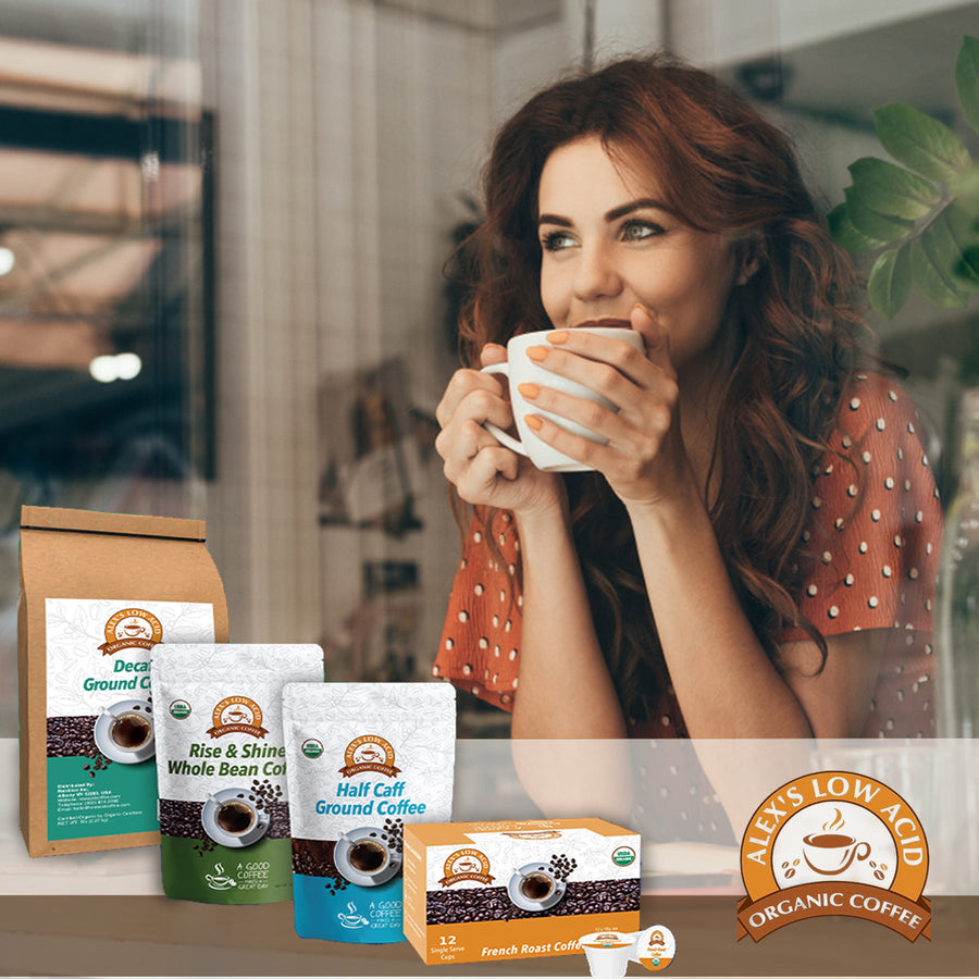 A woman with wavy brown hair smiles while holding a white coffee cup, sitting in a cozy café with various coffee products displayed in front of her.