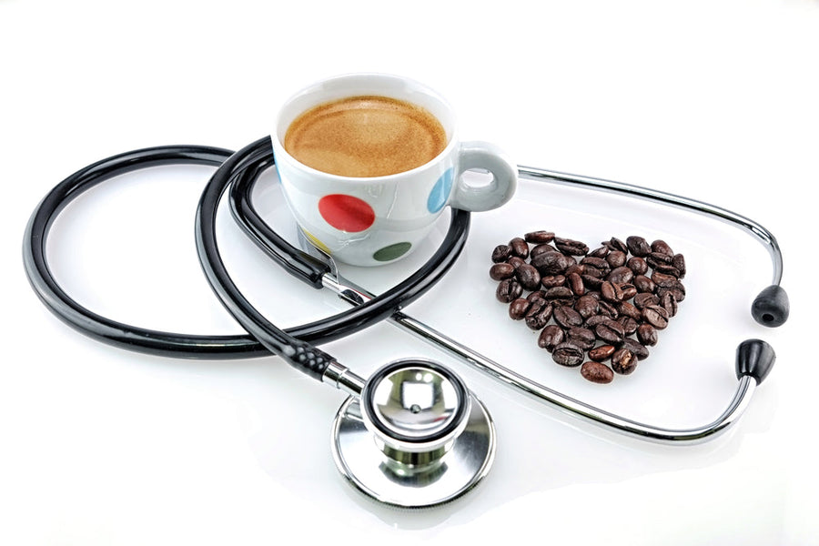 A coffee cup sits next to a stethoscope, with coffee beans arranged in a heart shape, symbolizing a connection between health and coffee.