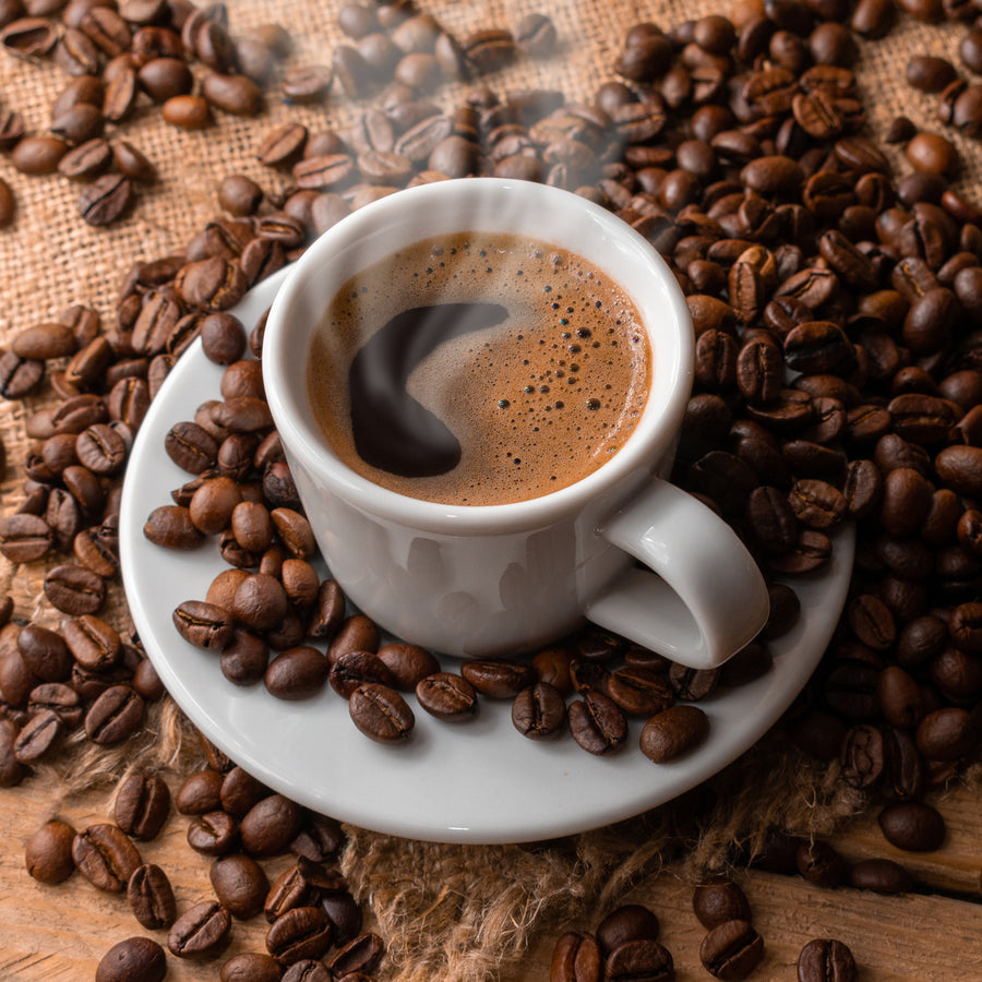 A steaming cup of coffee sits on a white saucer, surrounded by scattered coffee beans on a rustic wooden surface, creating a cozy and inviting atmosphere.