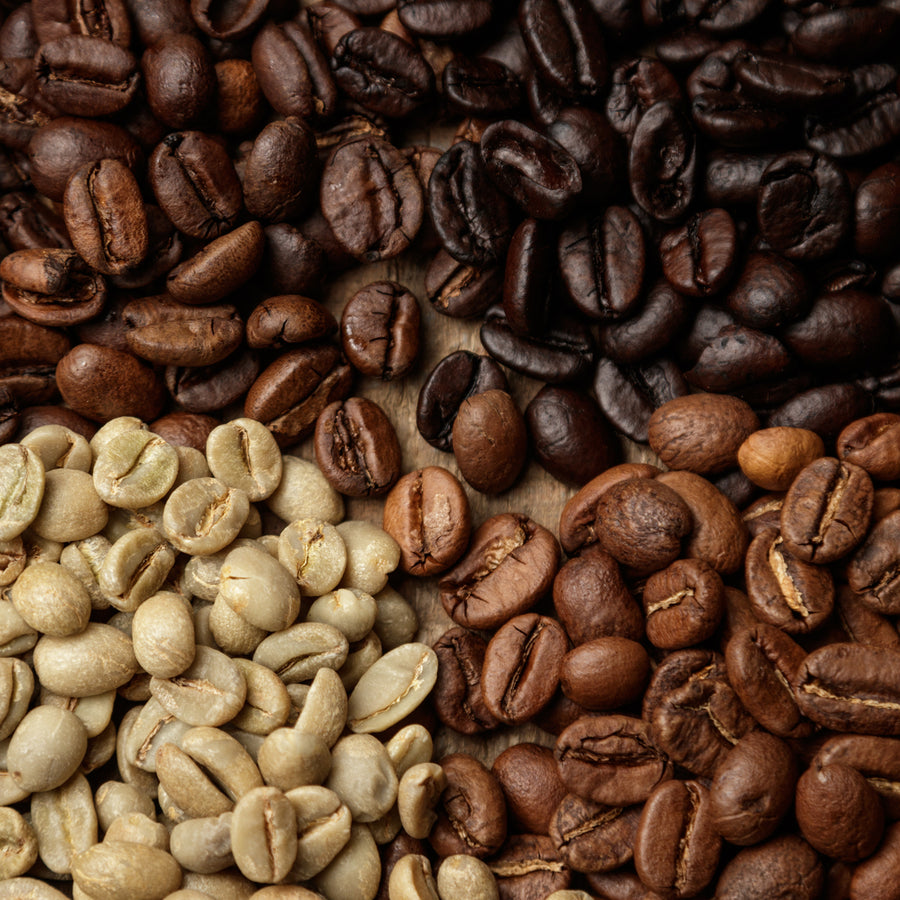 Various types of coffee beans are arranged in four sections on a wooden surface, showcasing their different colors from light green to dark brown, highlighting the roasting process.