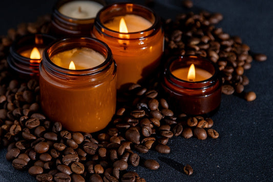 Four candles with flickering flames are arranged among scattered coffee beans on a dark surface, creating a warm and inviting atmosphere.