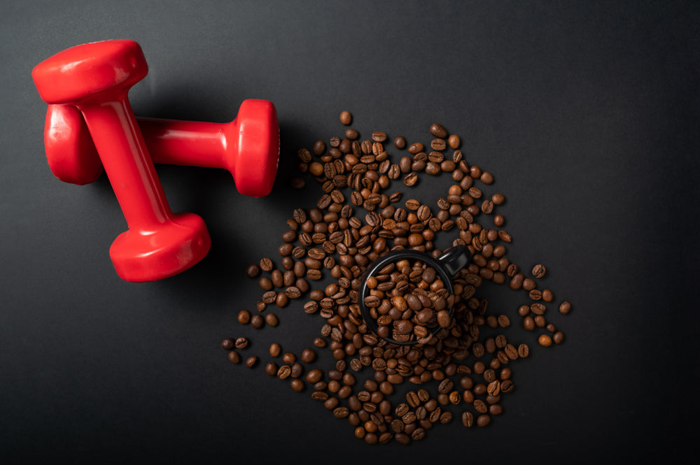 Two red dumbbells rest beside a black cup filled with coffee beans, which are scattered across a dark surface, creating a contrast between fitness and coffee culture.