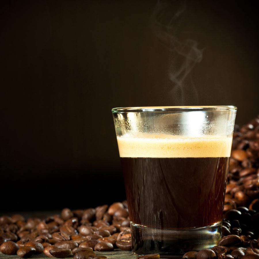 A steaming glass of dark coffee sits on a wooden surface surrounded by scattered coffee beans, highlighting a rich and inviting beverage.