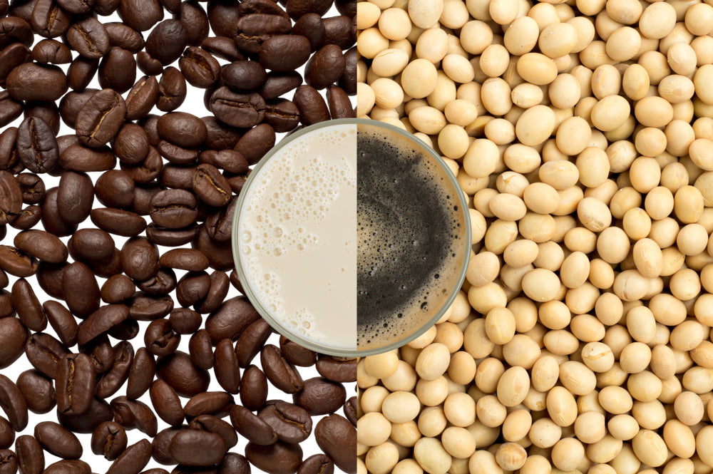 A glass of creamy coffee sits in the center, surrounded by dark roasted coffee beans on the left and light-colored soybeans on the right, highlighting a contrast between the two ingredients.