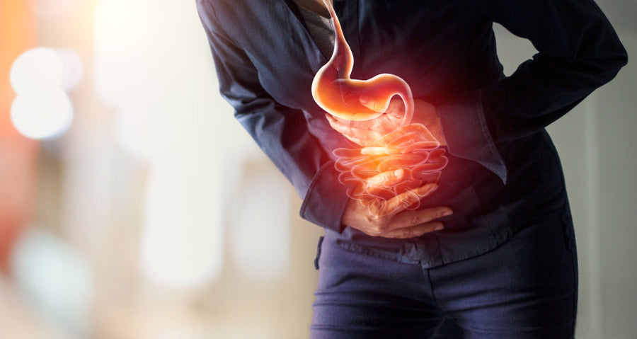 A person in a dark shirt is holding their stomach in discomfort, with a glowing graphic of the digestive system superimposed to illustrate the pain in a clinical setting.