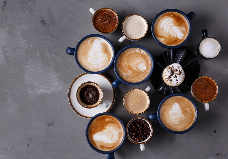 A variety of coffee cups, featuring latte art and different coffee types, are arranged on a gray surface, showcasing intricate designs and rich colors.