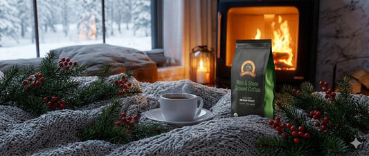 Alex’s Low Acid Rise & Shine Ground Coffee beside a warm cup of coffee in a cozy winter living room with a fireplace and snowy view