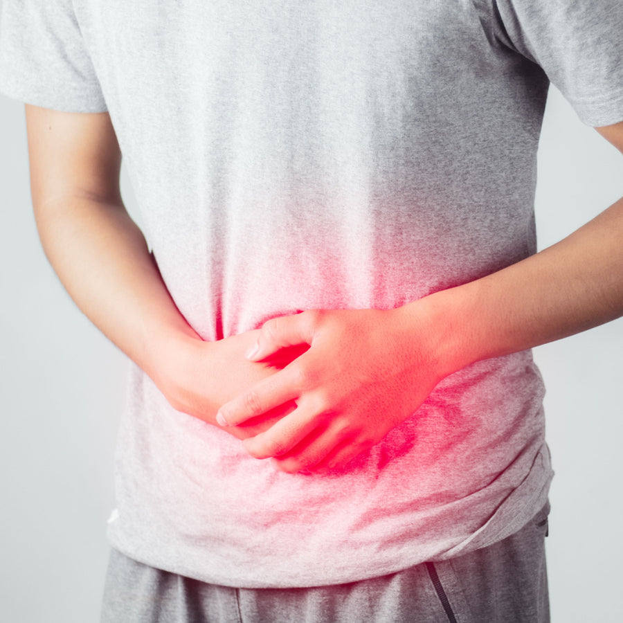 A person in a gray t-shirt is holding their stomach with both hands, showing signs of discomfort, against a plain background with a red glow highlighting the area of pain.