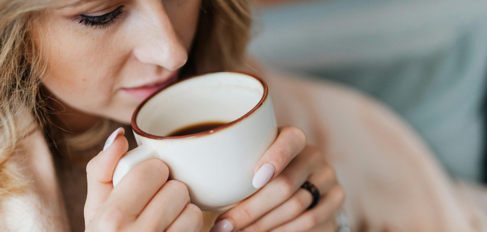 Woman holding a white mug with a dark liquid, possibly coffee or tea, in a cozy setting.