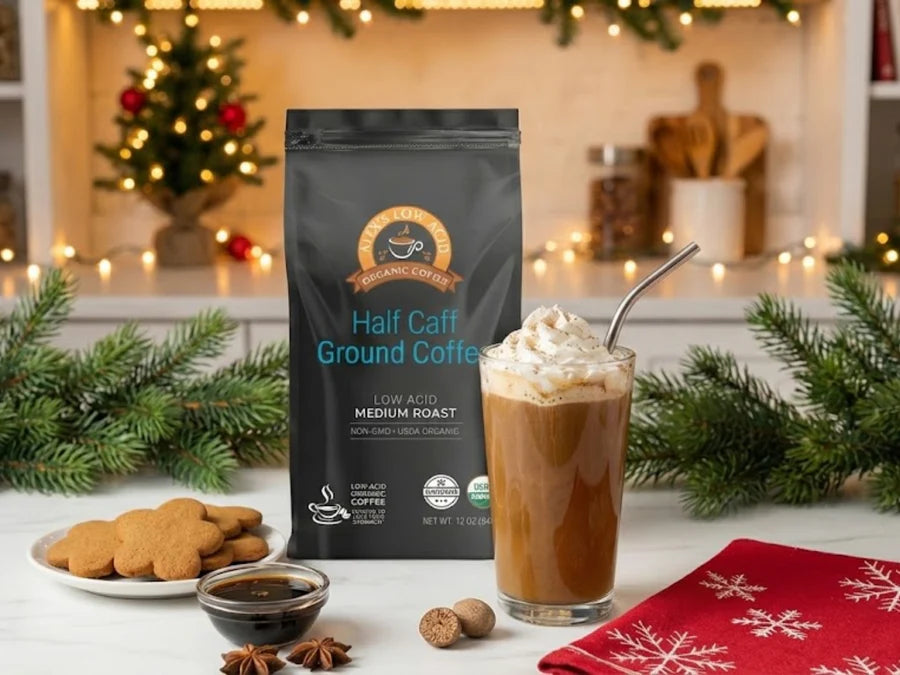 A bag of Half Caff Ground Coffee stands beside a glass of iced coffee topped with whipped cream, gingerbread cookies, and festive decorations in a cozy kitchen setting.