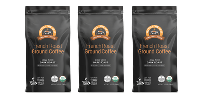 Three black bags of Alex's Low-Acid Organic Coffee™ - French Roast (12oz) from Alex's Low Acid Coffee are lined up, each with an orange and white label stating "Low Acid, Dark Roast, Non-GMO, USDA Organic"—ideal for low acid coffee enthusiasts.