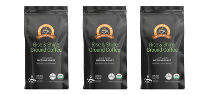 Three black bags of Alex's Low-Acid Organic Coffee™ - Rise and Shine Fresh Ground (12oz) by Alex's Low Acid Coffee are displayed side by side, each featuring green and white text, brown-orange seals, USDA Organic certification, and a low-acid formula.