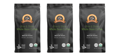 Three 12oz black bags of Alex's Low-Acid Organic Coffee™ - Rise and Shine Whole Bean by Alex's Low Acid Coffee, featuring low acid, medium roast, non-GMO labels, certification logos, and a coffee cup graphic on the front.